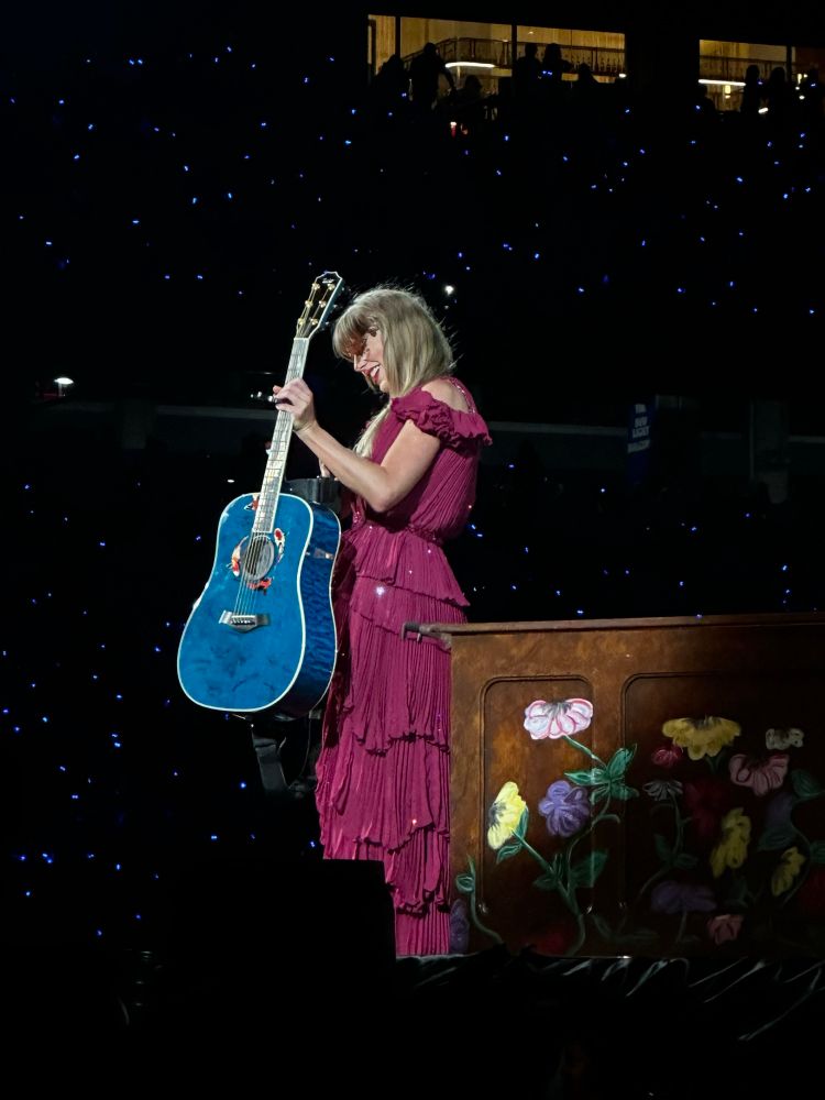 Taylor Swift on stage at the eras tour. She is starting the acoustic section. She’s brought out the koi fish guitar for the very first time. She’s wearing the original red dress. 