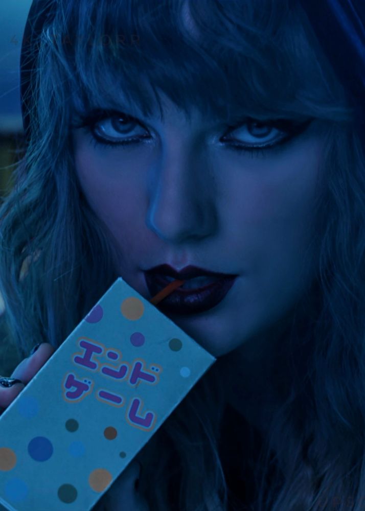 Taylor Swift in the End Game music video. She is sipping a juice box that has Japanese writing and polka dots on it. She has dark lipstick and eye makeup on and her hair is down surrounding her face. 