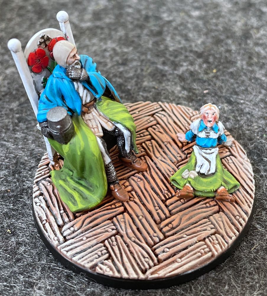 Two painted miniatures, one a knight in chainmail armor and tabard sitting on a chair, grey in his beard and a thoughtful expression, one a child sitting back on the floor nearby, wearing the same heraldric colours, screaming her little heart out. 
From this angle, the little girl is screaming Right at the viewer