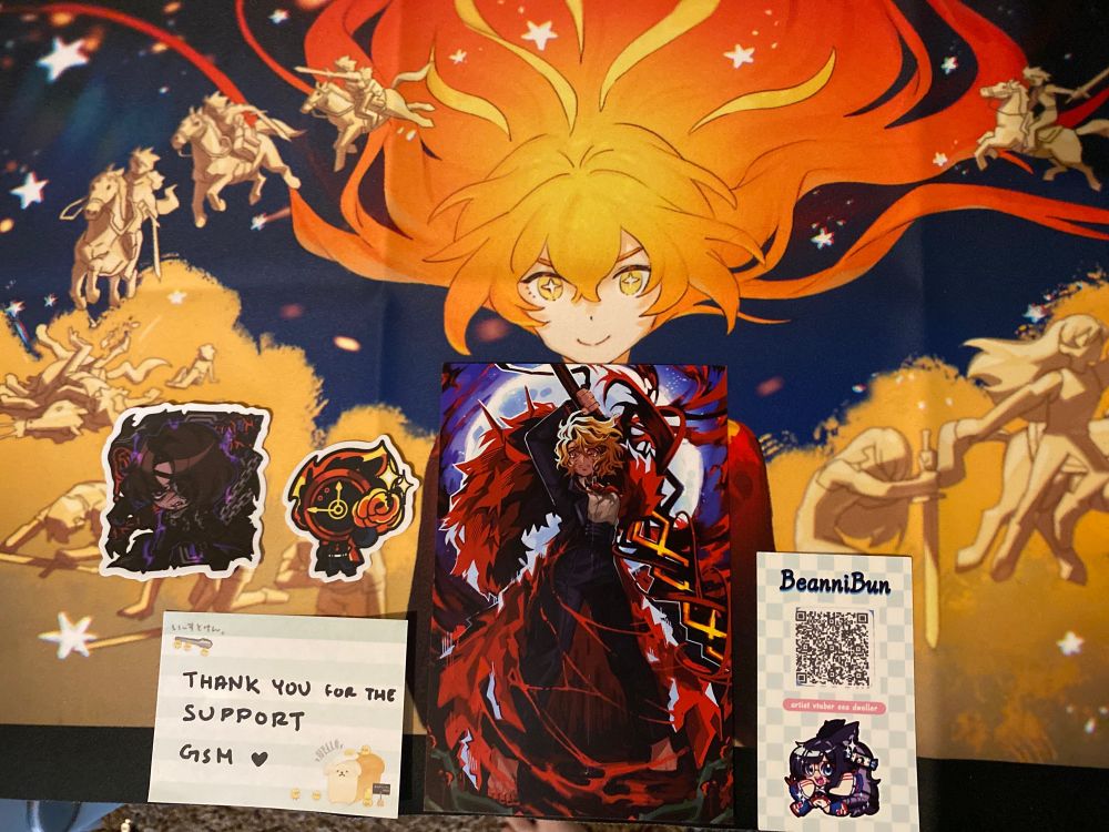 Behind the official Mili poster for “Hero”, there are two stickers for Wild Hunt Heathcliff and Dante from Limbus Company holding a stem of Lunacy. There is a hand-written note that says “thank you for the support GSM”, next to a print of Sancho from Limbus Company. BeanniBun’s QR code is on a card.