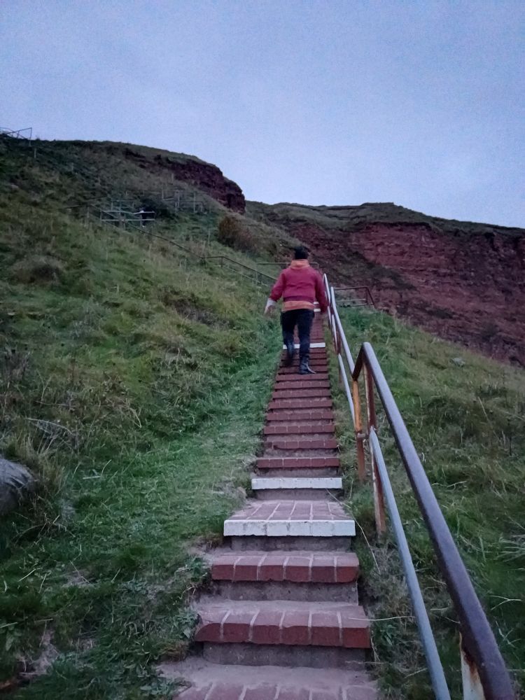 Mein Partner steigt die Treppe zu den Klippen hoch. Es ist Dämmerung und man sieht ihn von hinten 