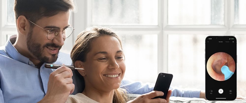 um home colocando o limpador de ouvido com câmera no ouvido da parceira enquanto ambos assistem à filmagem no celular como um curta de terror cósmico para tiktok