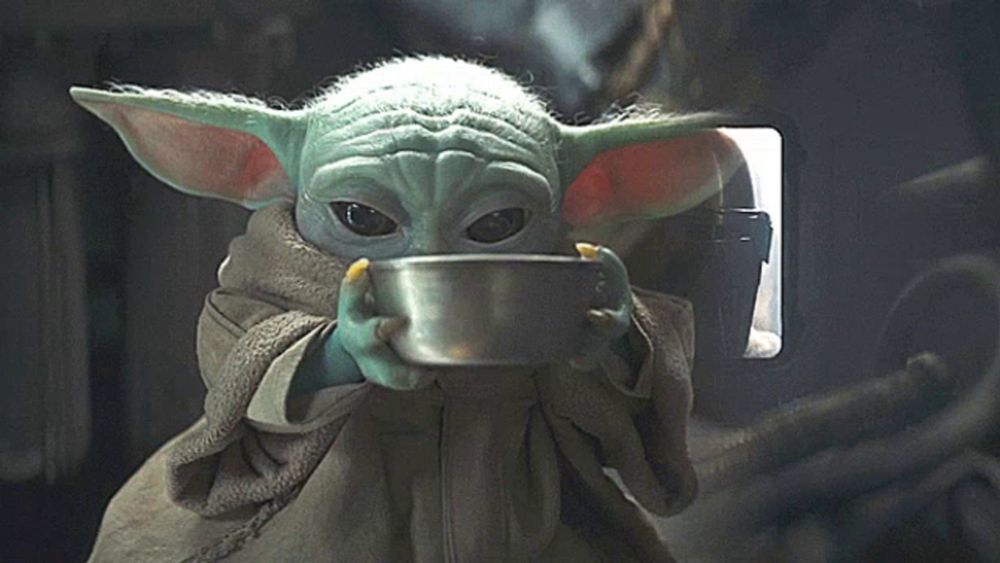 a baby yoda holding a bowl of food in his hand