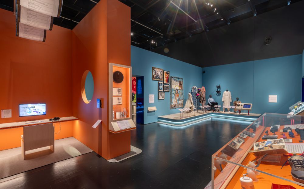 Wide shot of the Design & Disability exhibit at the South Kensington V&A. On the far left side is a corner nook with Unpacking on a computer screen