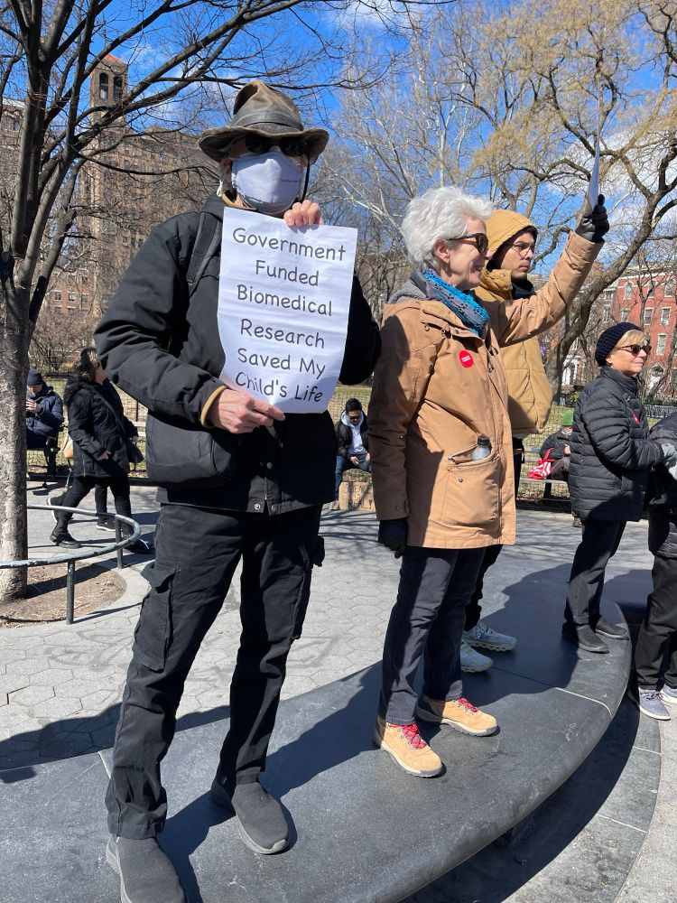 Men holding “Government funded biomedical research saved my child’s life” sign