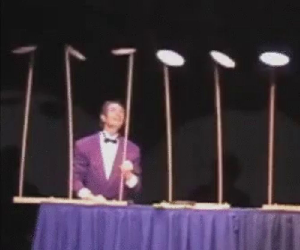 a man in a purple tuxedo is juggling plates on sticks on a stage