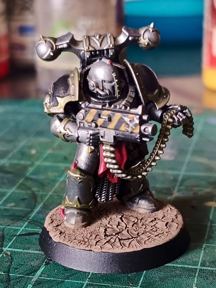 Painted model of an Iron Warriors Chaos Space Marine holding his boltgun in one hand and its ammo belt in the other.