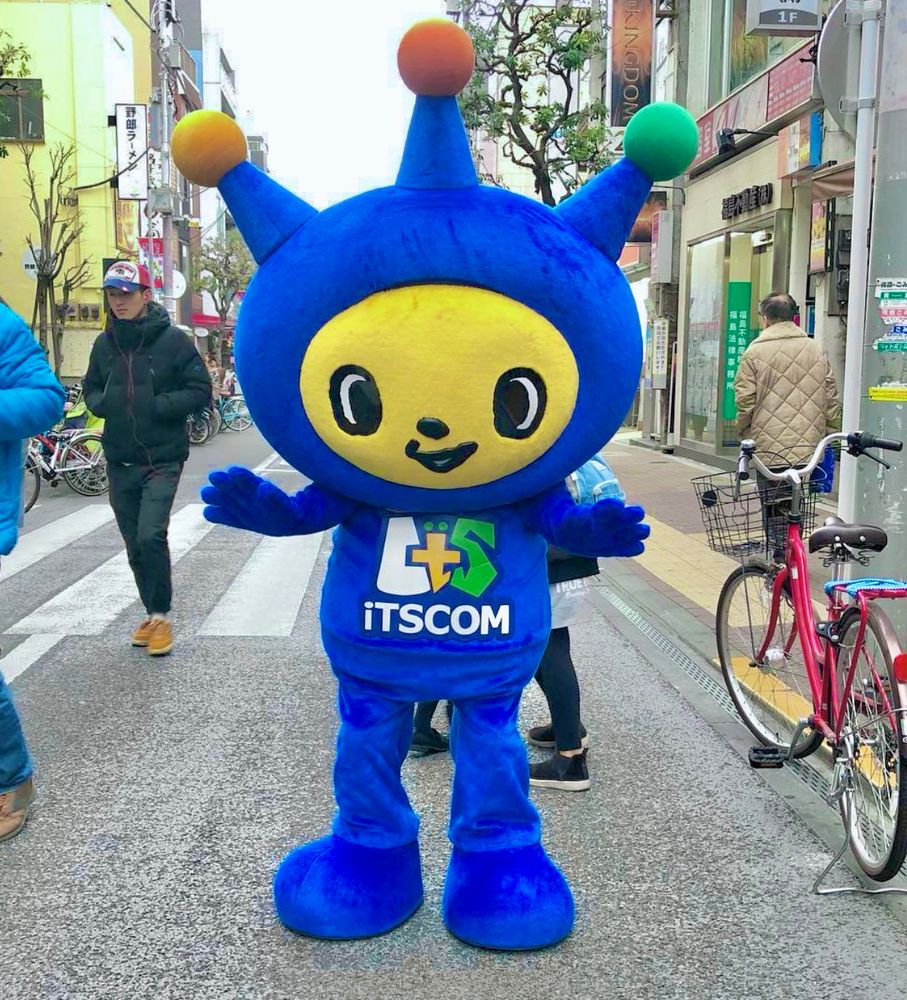 A blue alien mascot with three antennae stands in the street.