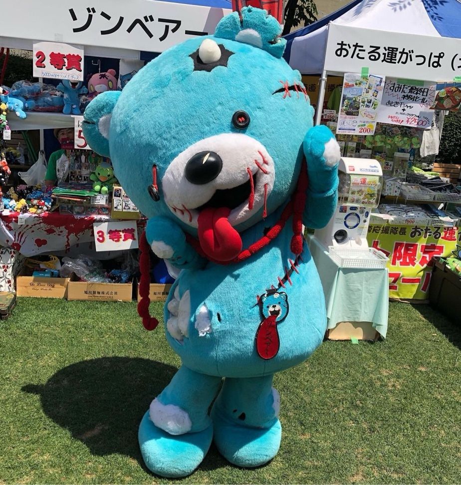 A blue teddy bear with rips and tears on it and an eye hanging off holds a string of intestines.