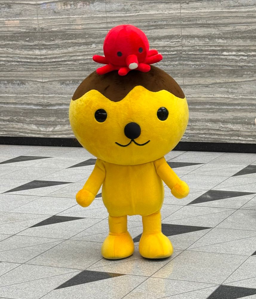 An orange mascot with a takoyaki squid ball for a head and a little red squid sitting on top of it