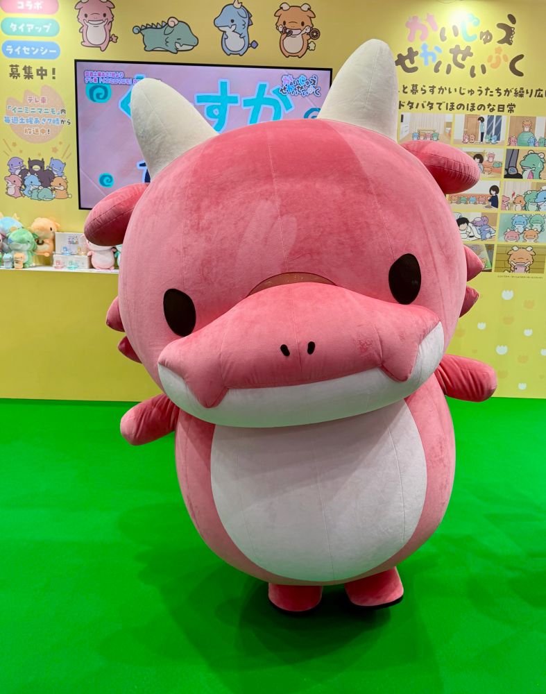 A pink dragon mascot stands on a green carpet