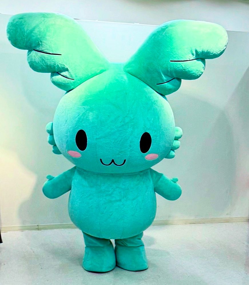 A turquoise, bunny-like mascot with ears that are wings
