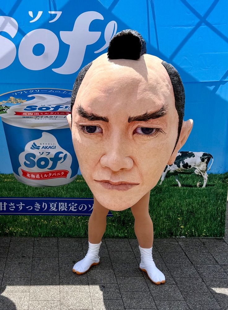 A realistic stoic head with a samurai topknot stands in two legs in front of an ad for ice cream.