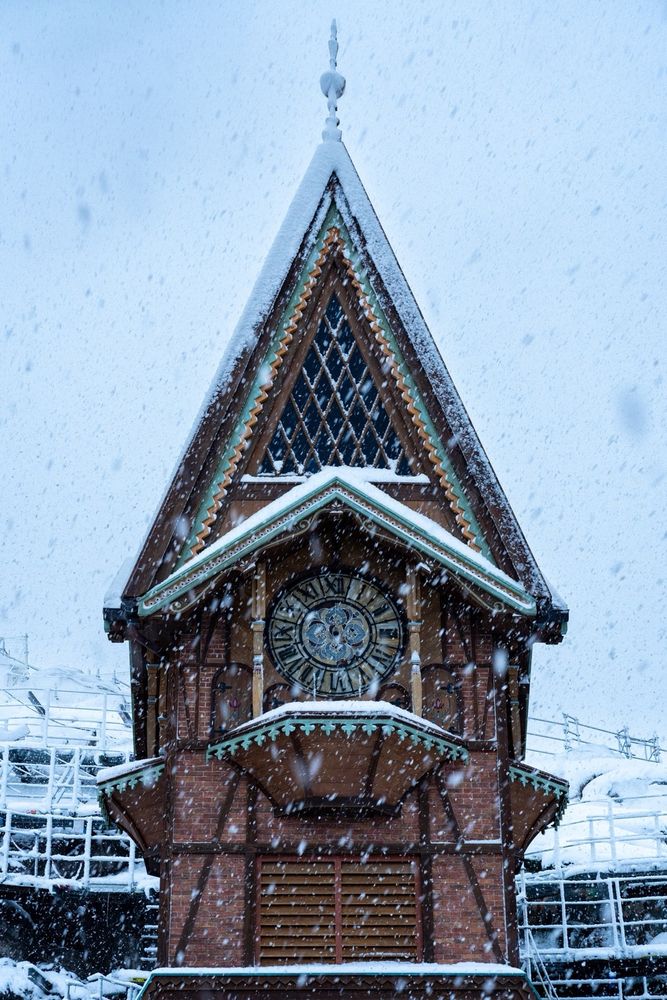 Another shot of the clock tower and scaffolding inside World of Frozen at Walt Disney Studios Park, covered in snow as more snow falls from the sky.