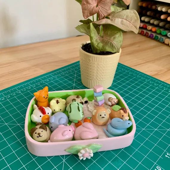 Photo of a pastel tray filled with handmade figurines representing the twelve Zodiac animals from Fruits Basket. The tray is placed on a green cutting mat, with a potted plant in the background.