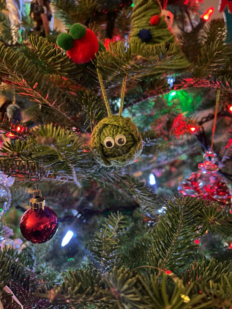 A knitted Brussels sprout with googly eyes hanging on a tree