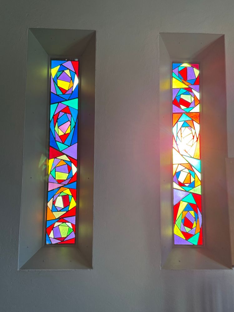 Two narrow colourful glass art windows with the sun shining through. 