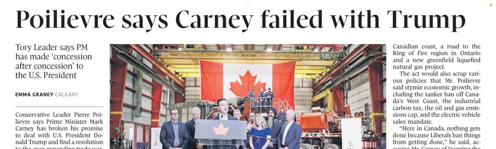 A group of officials stands in a workshop, with a large Canadian flag displayed prominently behind them.