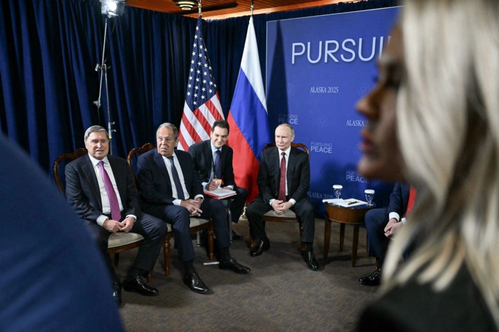 A group of officials seated in front of a backdrop featuring the flags of the U.S. and Russia, performatively discussing matters of 