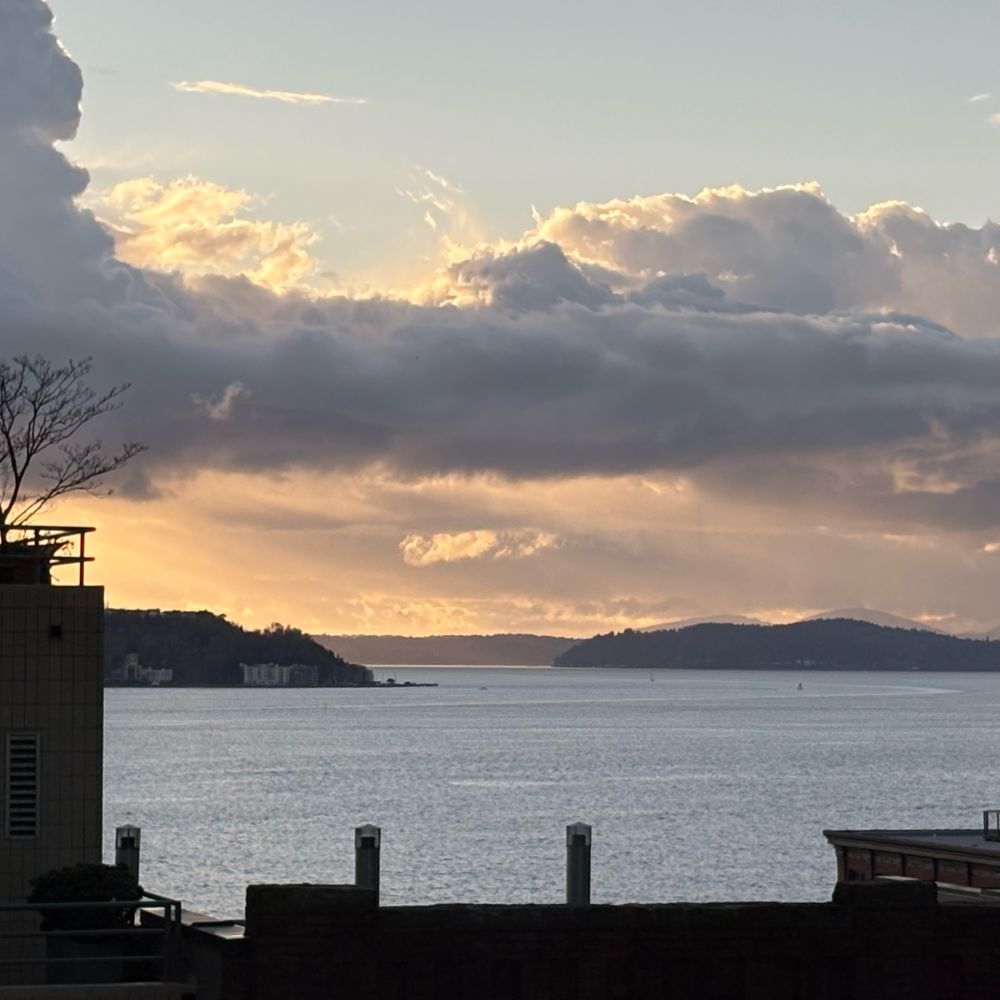 A view of Puget Sound from downtown Seattle. West Seattle is visible in the distance. The clouds are golden and gorgeous, lit with the impending sunset