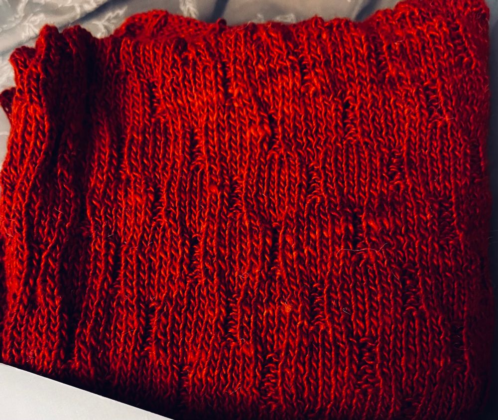 Deep crimson colored yarn, specifically a noro yarn, the sonata, colorway 43 chili. Knitting work in progress, a modified basketweave pattern 