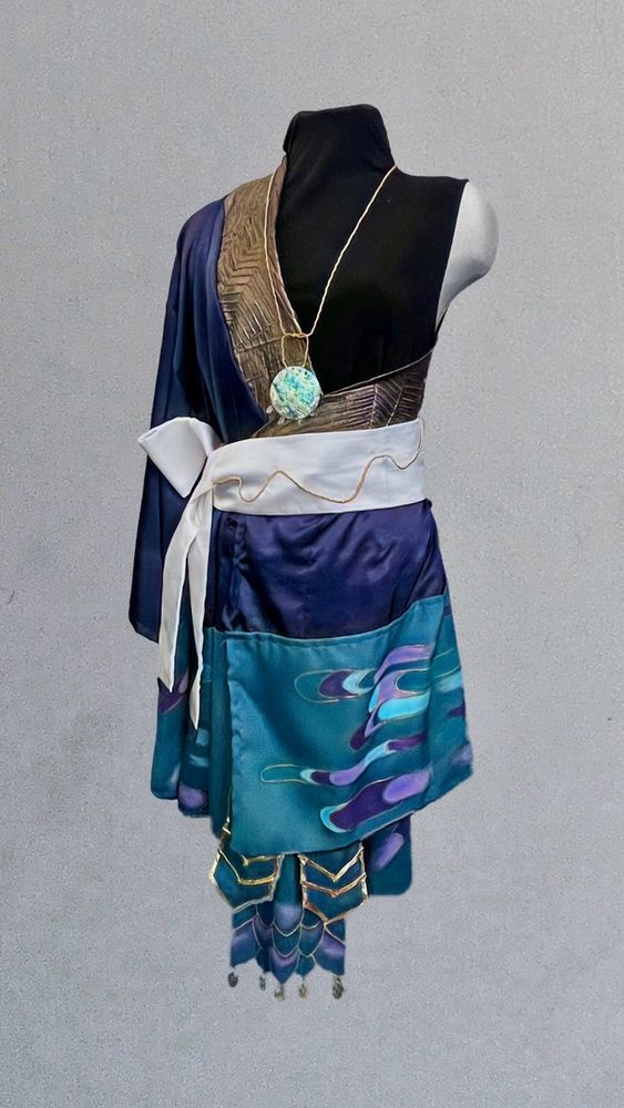 Blue satin kimono with teal fabric attached to the bottom. Teal fabric is painted with Japanese pattern with two shades of purple, light blue, and gold paint. White obi with gold wave like tie. Teal fabric panel with painted dragon scales outlined in gold. 