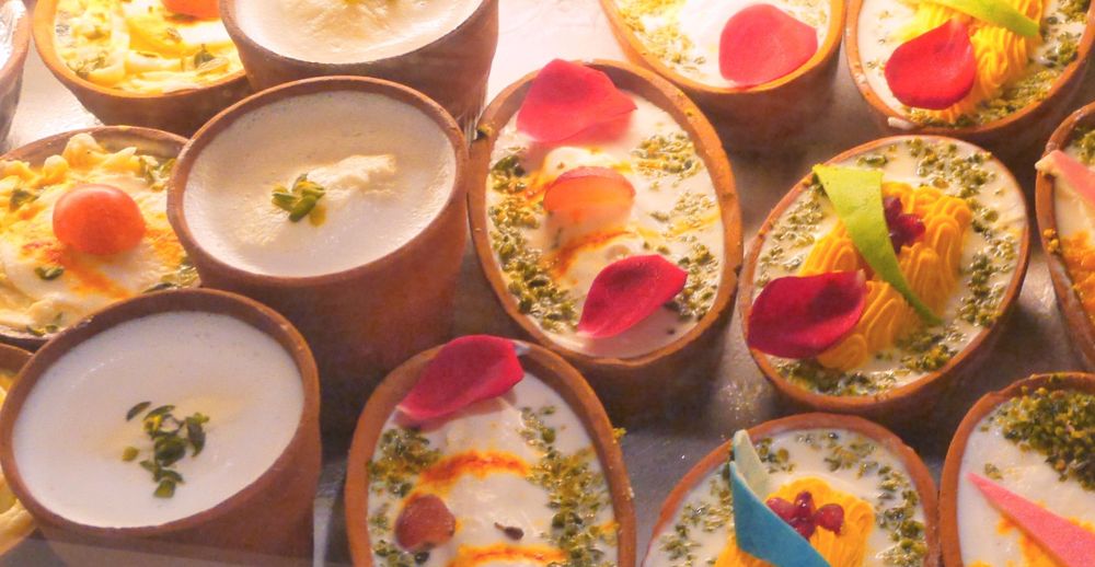 A symbolic picture showing a range of colorful milk-based desserts covered in flower pedals and pieces of fruits.
