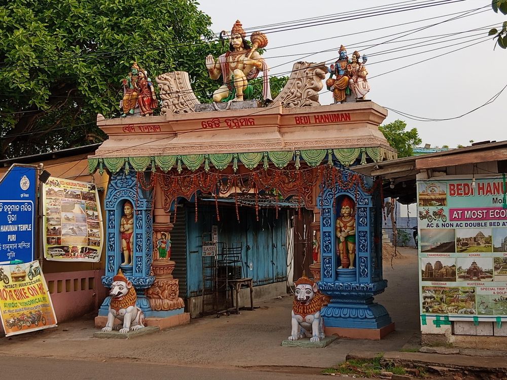 Colorful temple entrance featuring three Hanuman figures, as well as the "holy family" to its side. The big Hanuman is holding his iconic weapon in one hand, while raising his other hand in a warding posture, his palm points towards the sea.