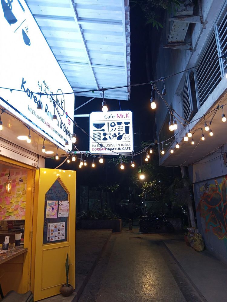 Picture of a narrow alley with hundreds of tiny lamps and neon signs. An advert for "Mr. K" points out an "exclusive Korean café"
