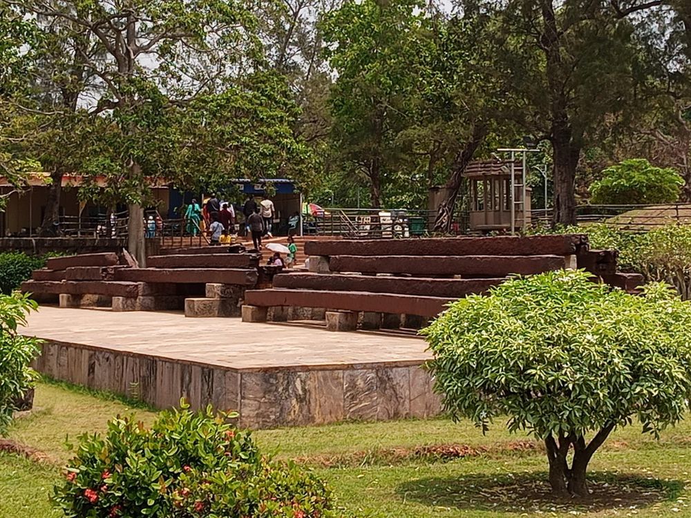 Broken rust-brown rectangular rods are suspended on stone benches in a garden for display