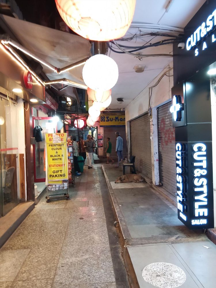 Picture of a narrow alley with hundreds of tiny lamps and neon signs. The adverts promise a "clinic", "automobiles", and "chai".
