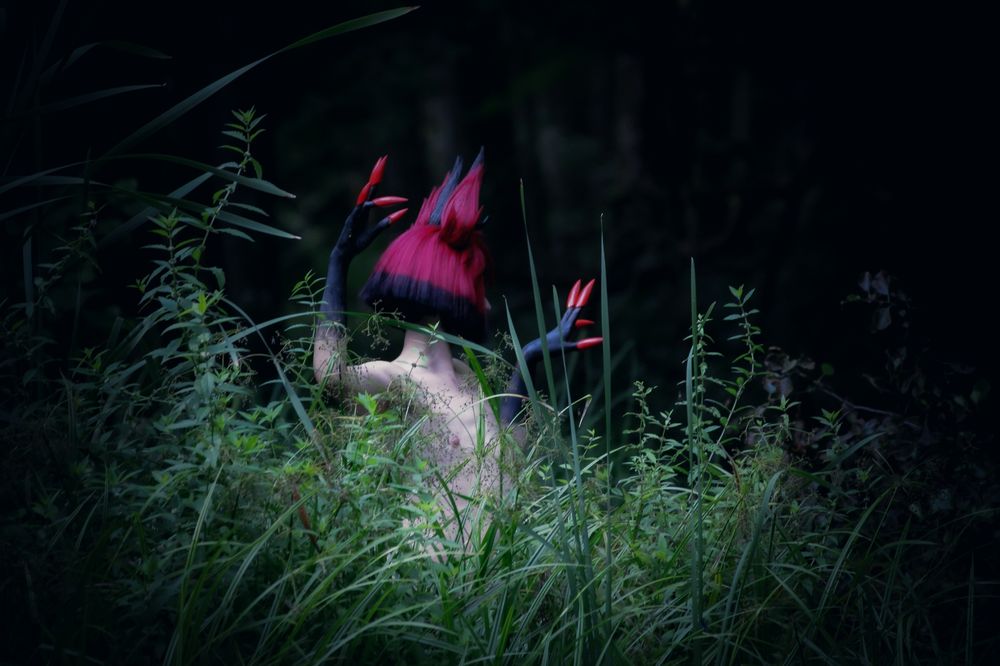 Alastor, a character from hazbin hotel, is standing behind plants without clothes, dark aesthetic 