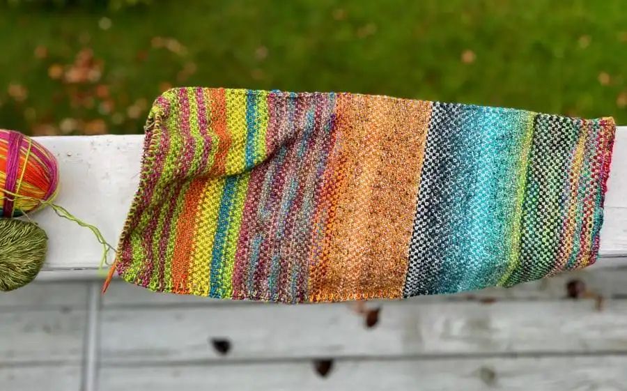 Colorful striped scarf in linen stitch and the two current balls of sock yarn to the left of the photo.