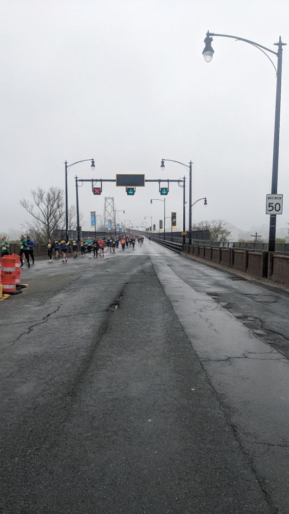 Two lanes of runners running down the MacDonald bridge on a foggy day.