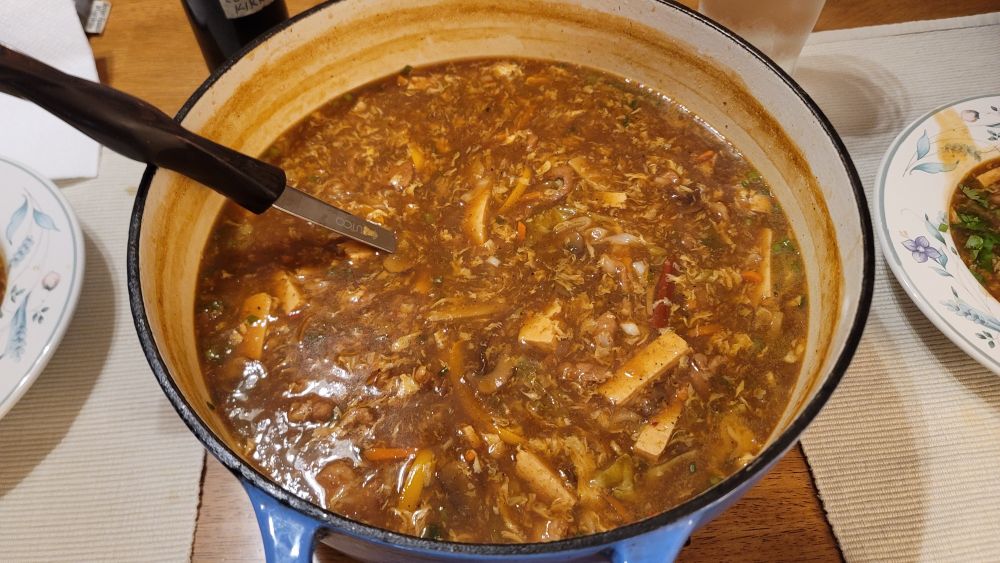 A large blue enameled cast iron pot filled with steaming hot soup. You can see floating slices of tofu, bamboo shoot, cabbage, carrot and mushroom.