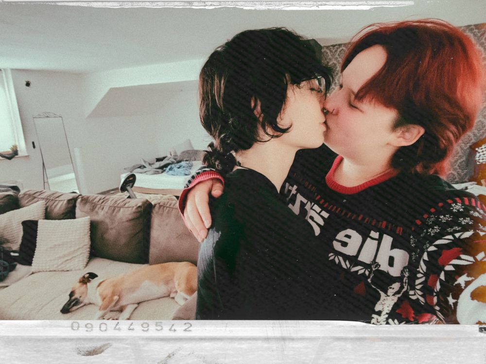 Mein Freund und ich, küssend, im Hintergrund auf dem Sofa ein Mittelgroßer, schlafender Hund.