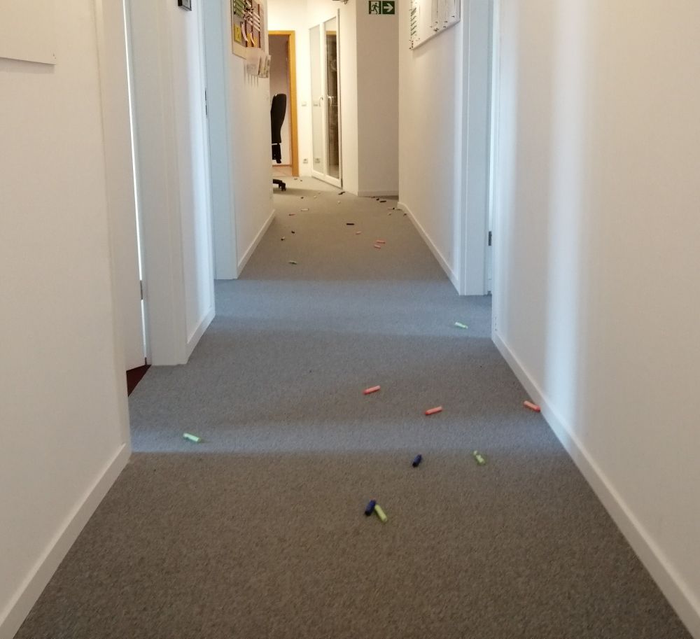 Ein Flur, in dem eine Menge Schaumstoff-Pfeile von Nerf-Blastern herumliegen. Weiter hinten steht ein Bürostuhl.
