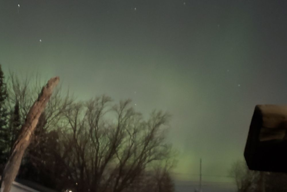 image is a photo of the sky with green aurora sheets across the horizon