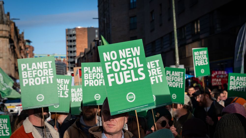 Green placards read "no new fossil fuels" and "planet before profit"