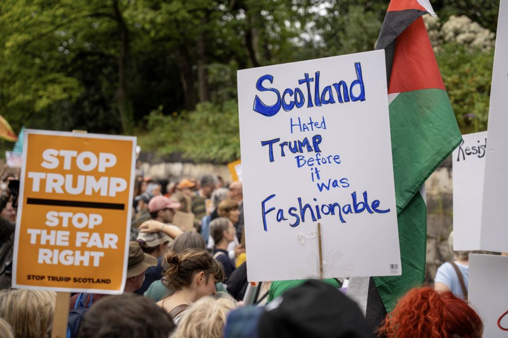A large group of protestors against Trump in Edinburgh. Two signs are visible, one reading 'Scotland hated Trump before it was fashionable', the other reading 'Stp Trump, stop the far right.'