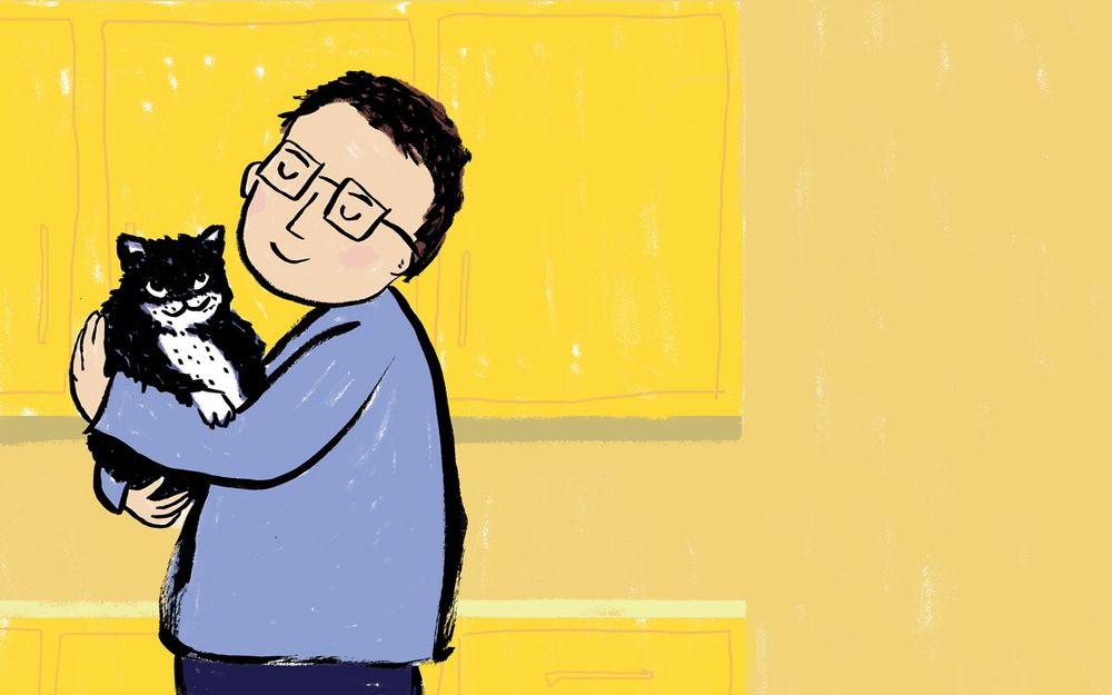 Man holding a big squishy tuxedo cat in a yellow kitchen.