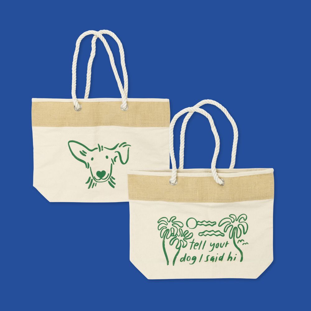 a canvas tote with rope straps has a green illustration of a dog's face on one side. the other side features a green illustration of a beach scene with "tell your dog i said hi."