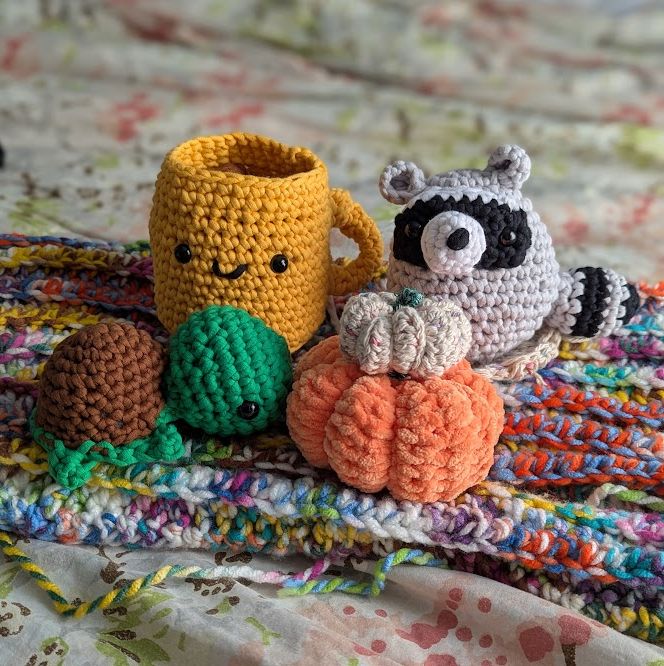 b's handmade crochet collection, including three woobles - a coffee mug with smiley, a raccoon, and a turtle, two pumpkins and a multicolored work in progress