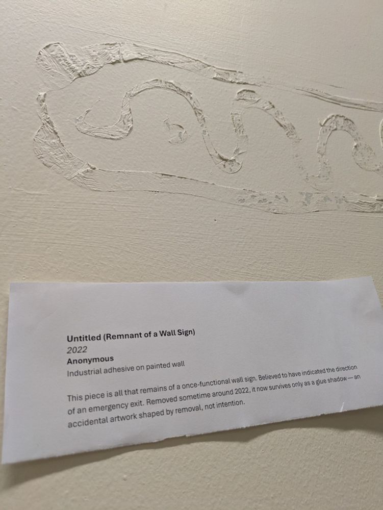 A mark on a wall with a joke museum-style description attached underneath.
