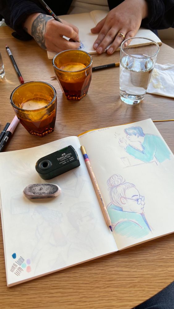 An artists sketchbook on a cafe table with some finished coffee drinks and drawing tools