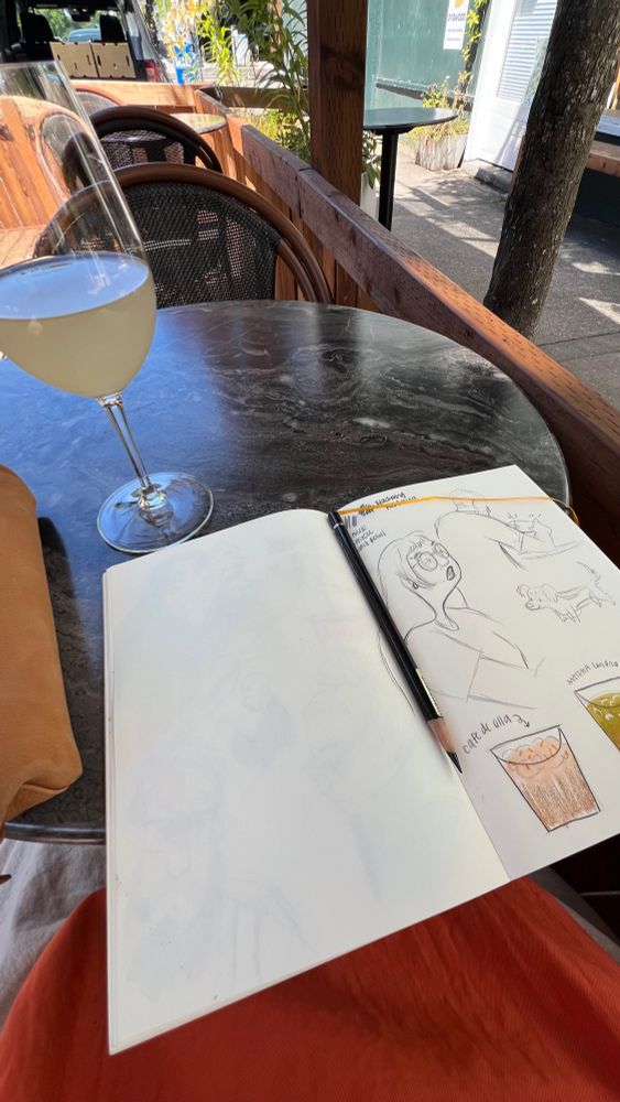 A sketchbook on a cafe table with a glass of wine. 