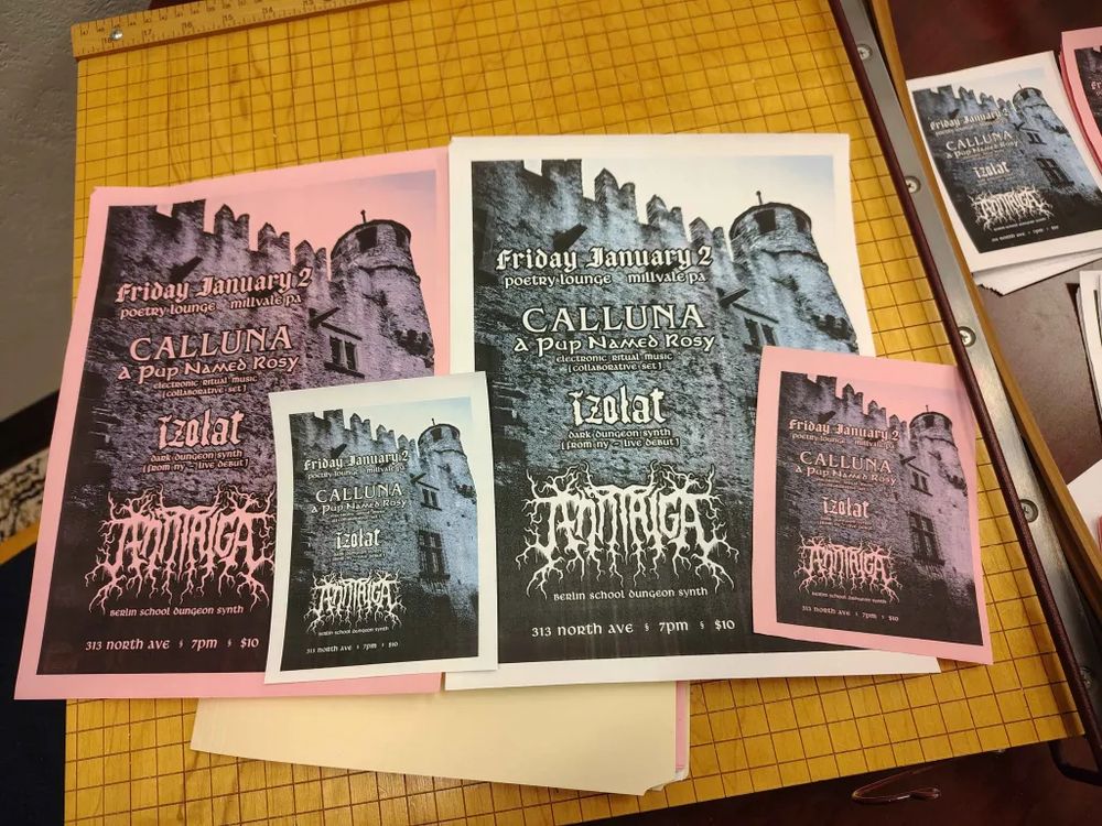 A paper cutter with four show flyers atop it, two large and two small, one of each being black and white and black and pink. Show flyer itself features the side of a castle with a tower. Text reads, "Friday January 2, Poetry Lounge, Millvale PA, Calluna+A Pup Named Rosy (electronic ritual music, collaborative set), Izolat (dark dungeon synth from NY, live debut), Jenn Taiga (Berlin school dungeon synth), 313 North Ave, 7 PM, $10