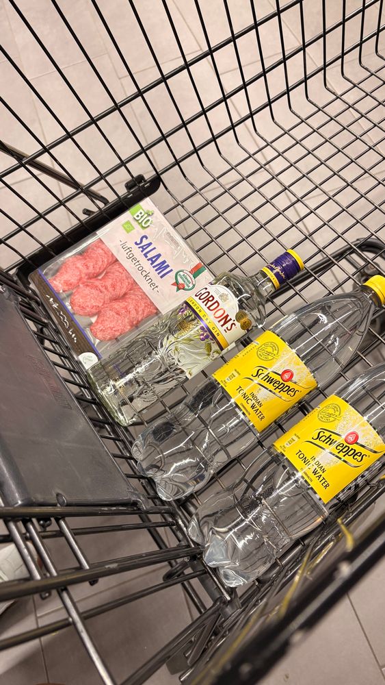 Ein Einkaufswagen mit einer Packung Bio-Salami, einer Flasche Gordon’s Dry Gin und zwei Flaschen Schweppes Indian Tonic Water.