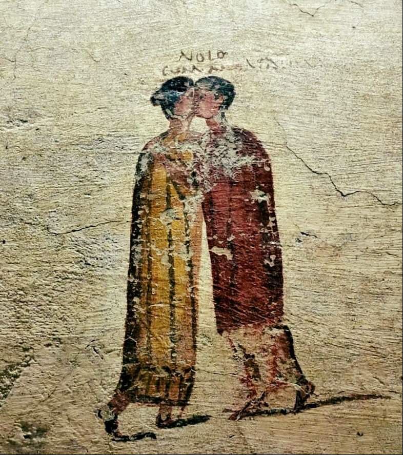 A woman in a long yellow dress holds hands with and kisses a man clad in red. The piece has a cartoonish feel to it.