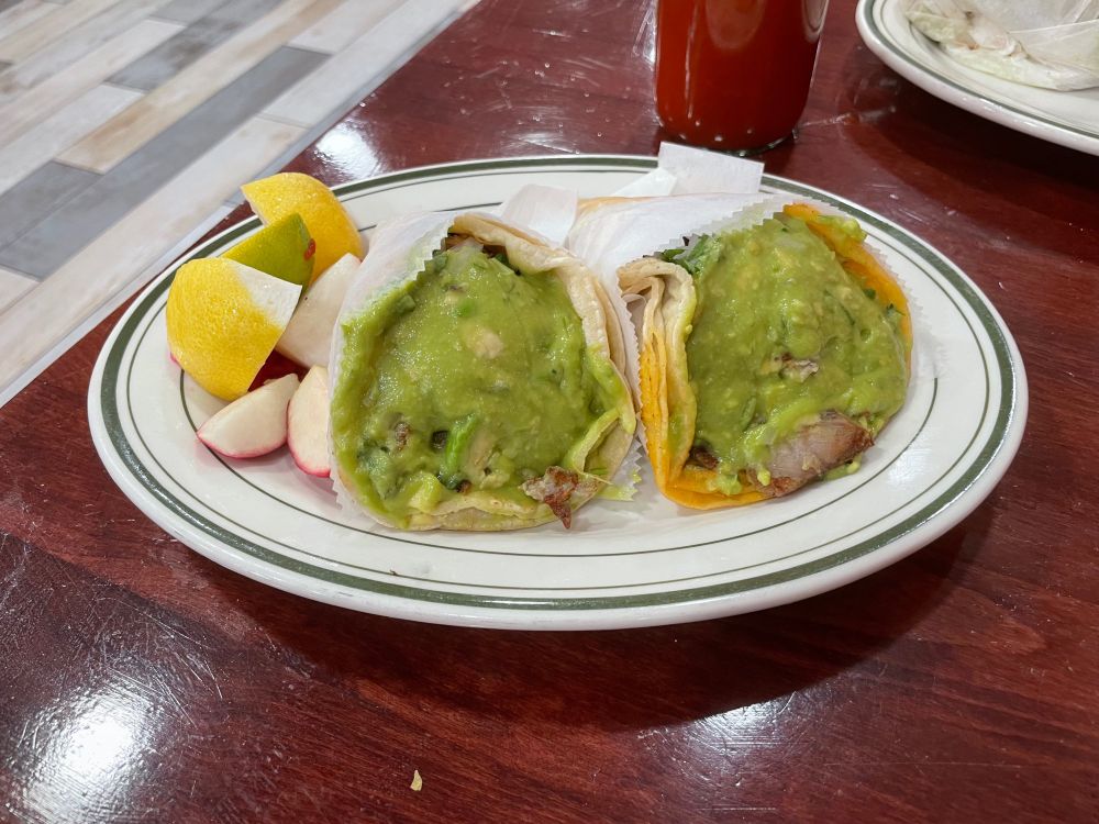 2 Tijuana style tacos on a plate with lemon and radish wedges on one side